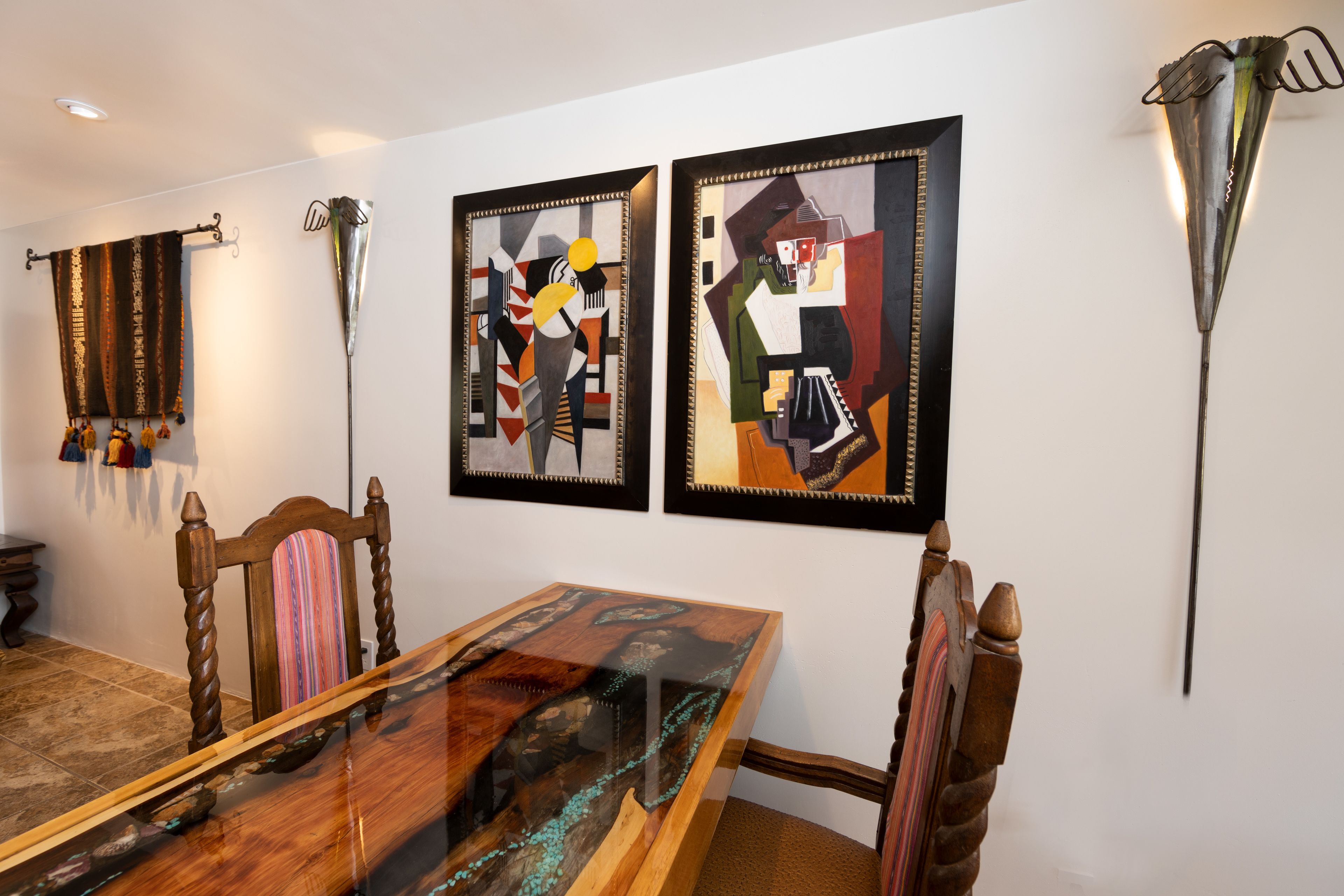 A dining area with a glass-top table, wooden chairs, and abstract art on the wall.