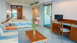 A hotel room with a bed, sofa, desk, TV, and a vase with flowers.