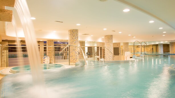 An indoor swimming pool with multiple water jets, a tiled floor, and a ceiling with recessed lighting.