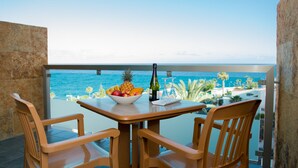 A balcony with a wooden table and chairs, a bowl of fruit, a bottle, and wine glasses.