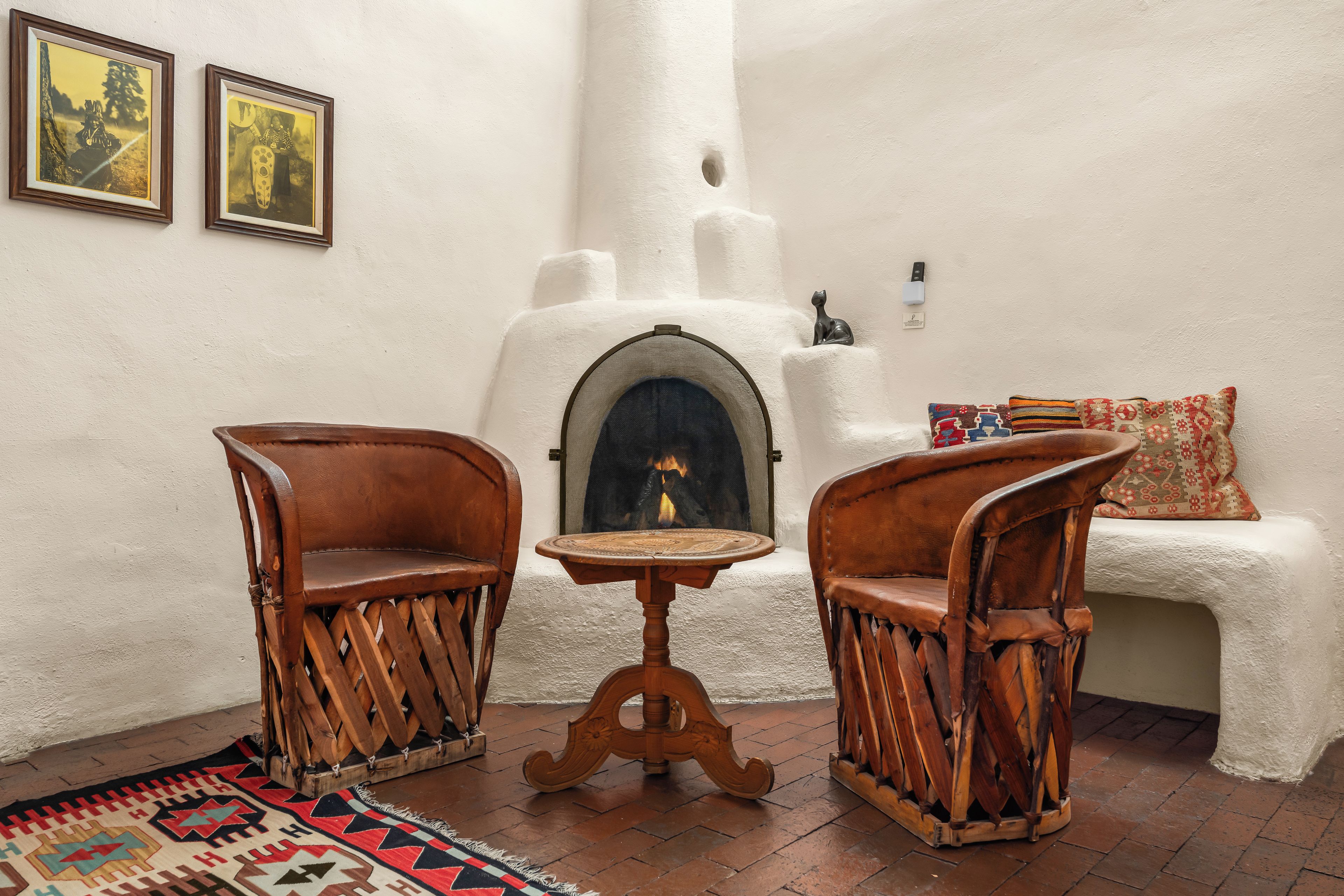 A room with two wooden chairs, a small round table, a fireplace, and a patterned rug.