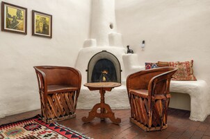 Una habitación con dos sillas de madera, una mesita redonda pequeña, una chimenea y un tapete estampado.