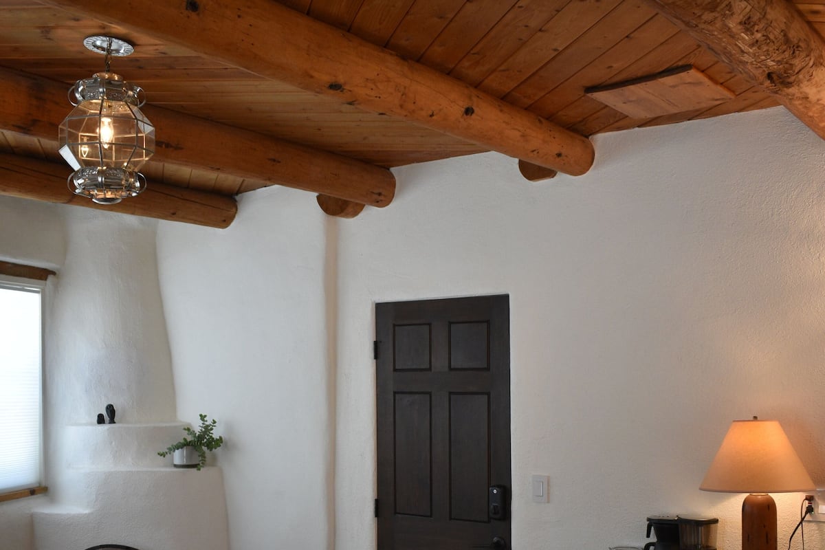 Un salon chaleureux avec une cheminée, des poutres apparentes en bois au plafond, un canapé, une table basse et un tapis à motifs.