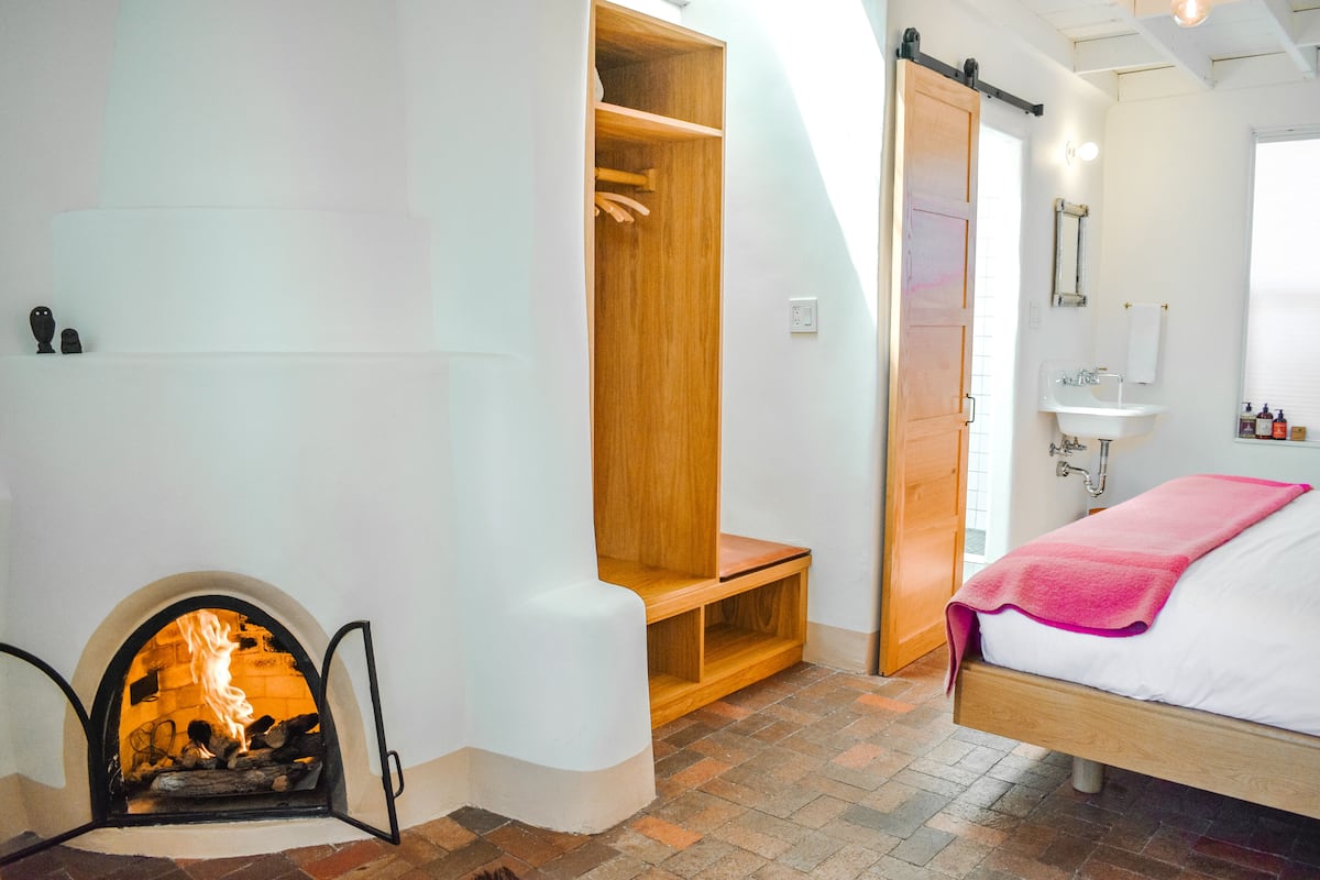 Une chambre avec une cheminée, une armoire en bois et un lit recouvert d’une couverture rose.