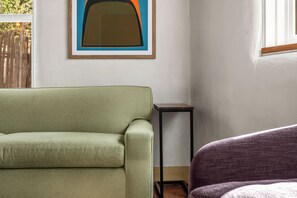 Una habitación con un sofá verde, una mesita negra pequeña y una silla morada.