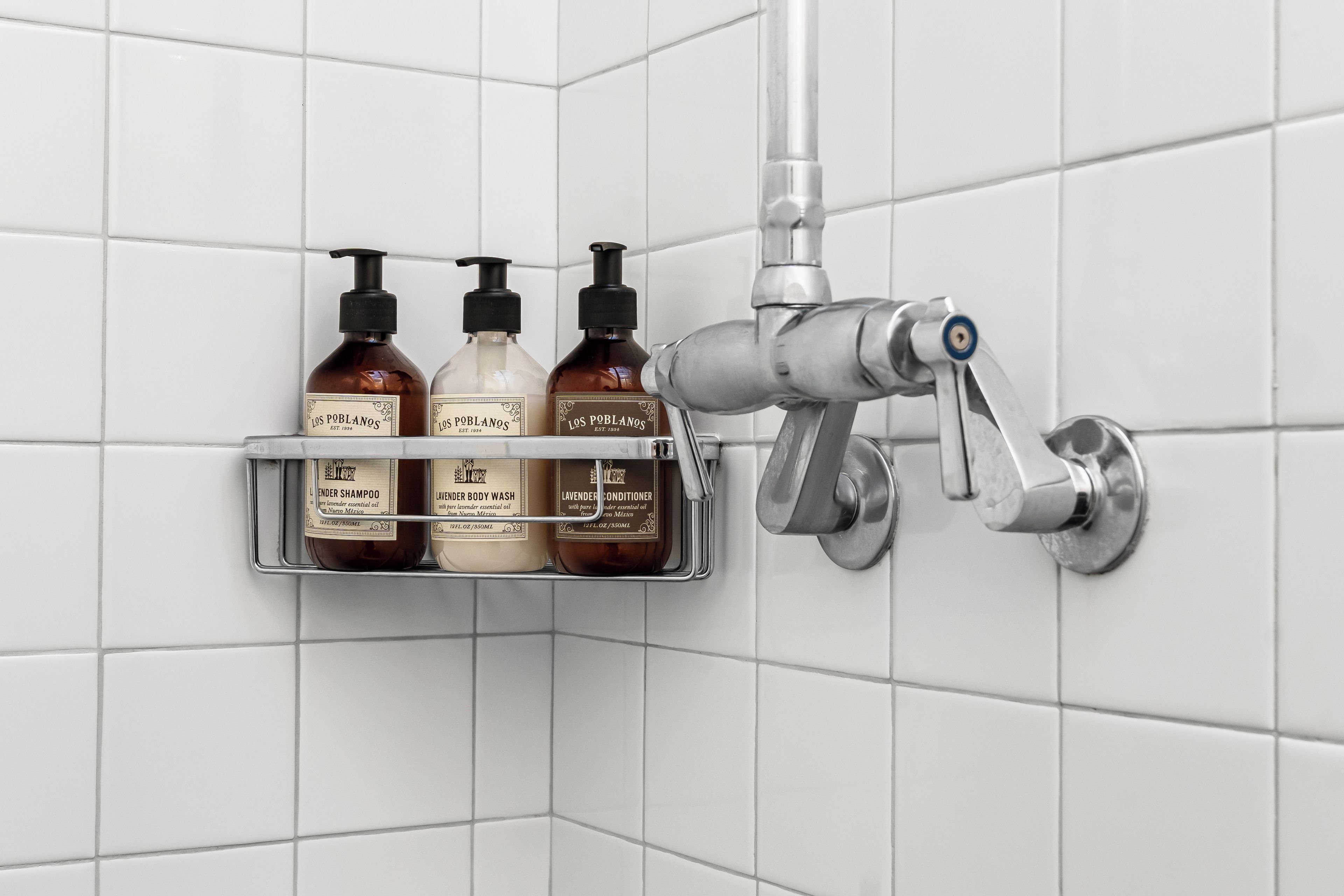 A bathroom corner with a shelf holding three bottles of Los Poblano products and a modern faucet.