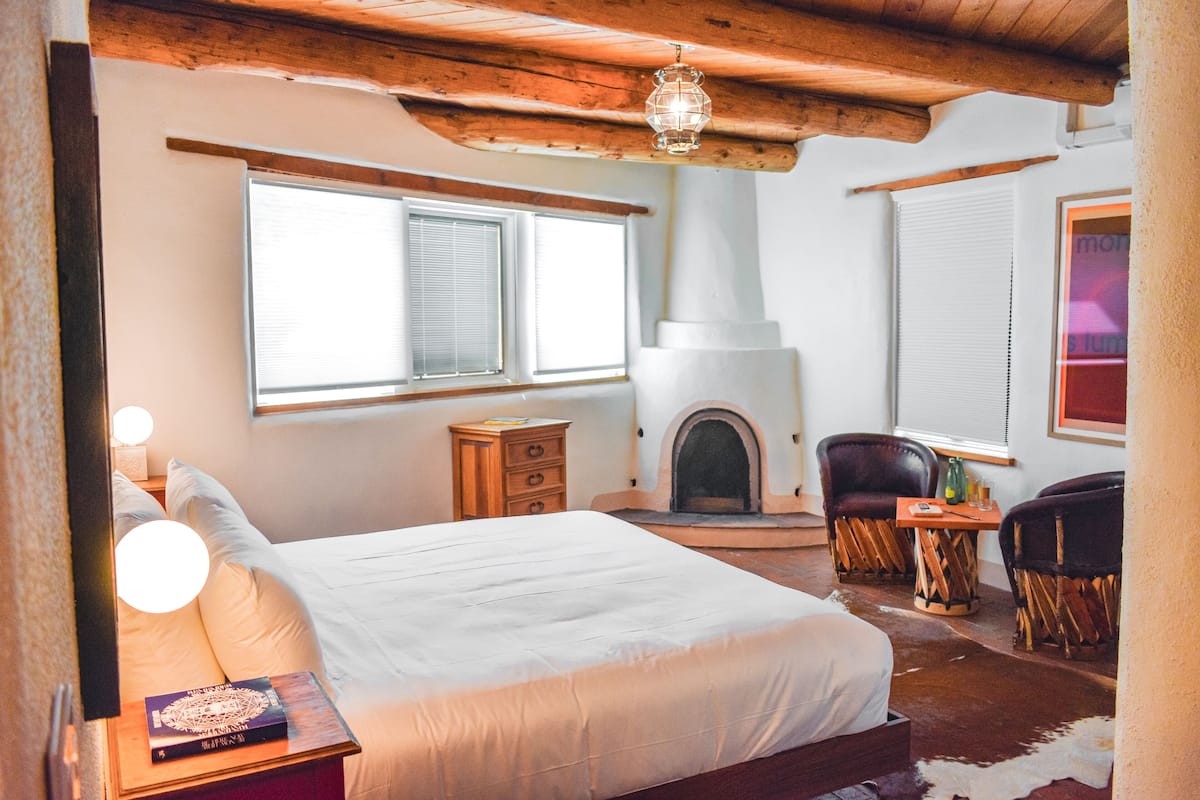 Une chambre confortable avec un grand lit, une commode en bois, une cheminée et deux fauteuils en cuir.