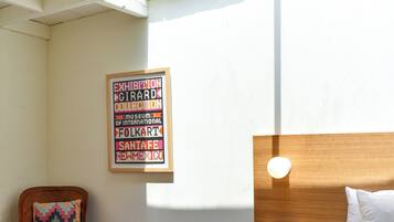 Et soveværelse med seng, natbord, stol, vægmonteret lampe og et indrammet billede.
