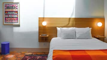 A hotel room with a wooden headboard, two bedside lamps, a bed with white linens, a colorful rug, and a framed sign on the wall.