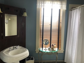 Une salle de bain avec un lavabo blanc, un miroir et une fenêtre avec des stores.