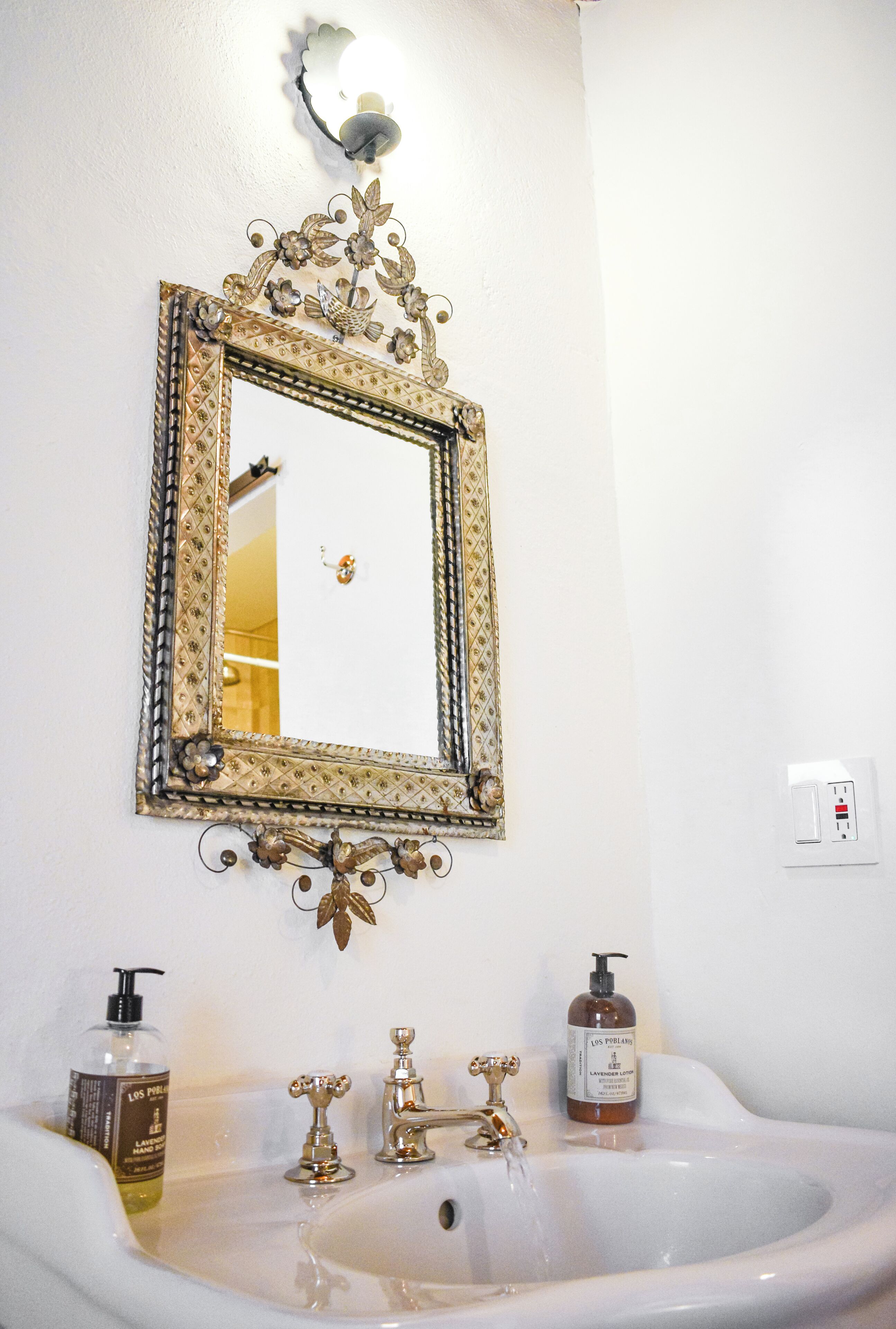 Een badkamer met een decoratieve spiegel, een wastafel en twee flessen lotion.