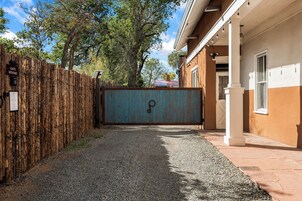 Una entrada protegida por un muro a una propiedad, con un camino de grava que conduce a un edificio de fachada marrón y portón azul.