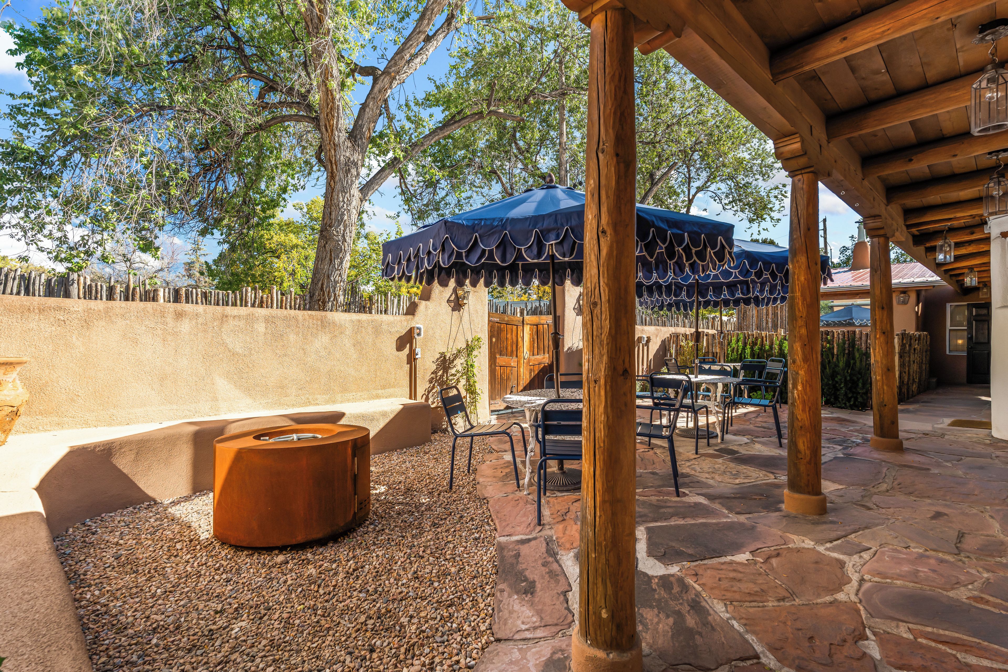 An outdoor patio with stone flooring, wooden tables and chairs, and a blue canopy.