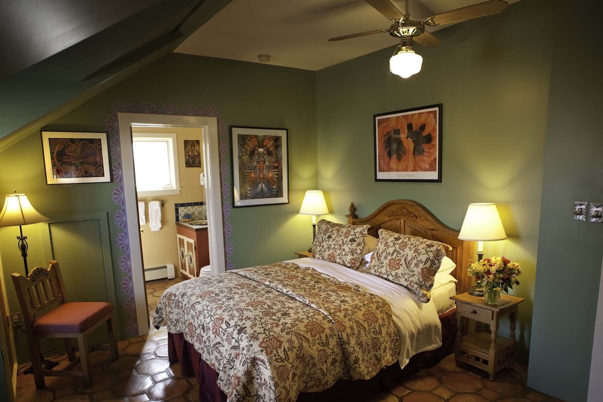 Une chambre à coucher avec un lit, deux tables de chevet avec des lampes, une chaise et un ventilateur de plafond.