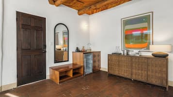 Een kamer met een houten deur, een bankje, een spiegel, een kast en een groot abstract schilderij.