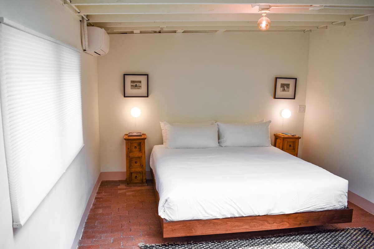Une chambre à coucher avec un lit en bois, deux tables de chevet, un radiateur blanc et deux lampes fixées au mur.