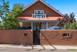 Una casa de dos pisos con balcón, puerta principal y acceso a través de una reja.