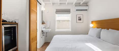A hotel room with a large bed, a wooden headboard, a television, a sink, and a window with blinds.
