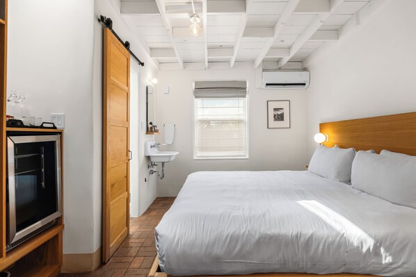 Una habitación de hotel con una cama grande, cabecera de madera, televisor, lavamanos y una ventana con persianas.
