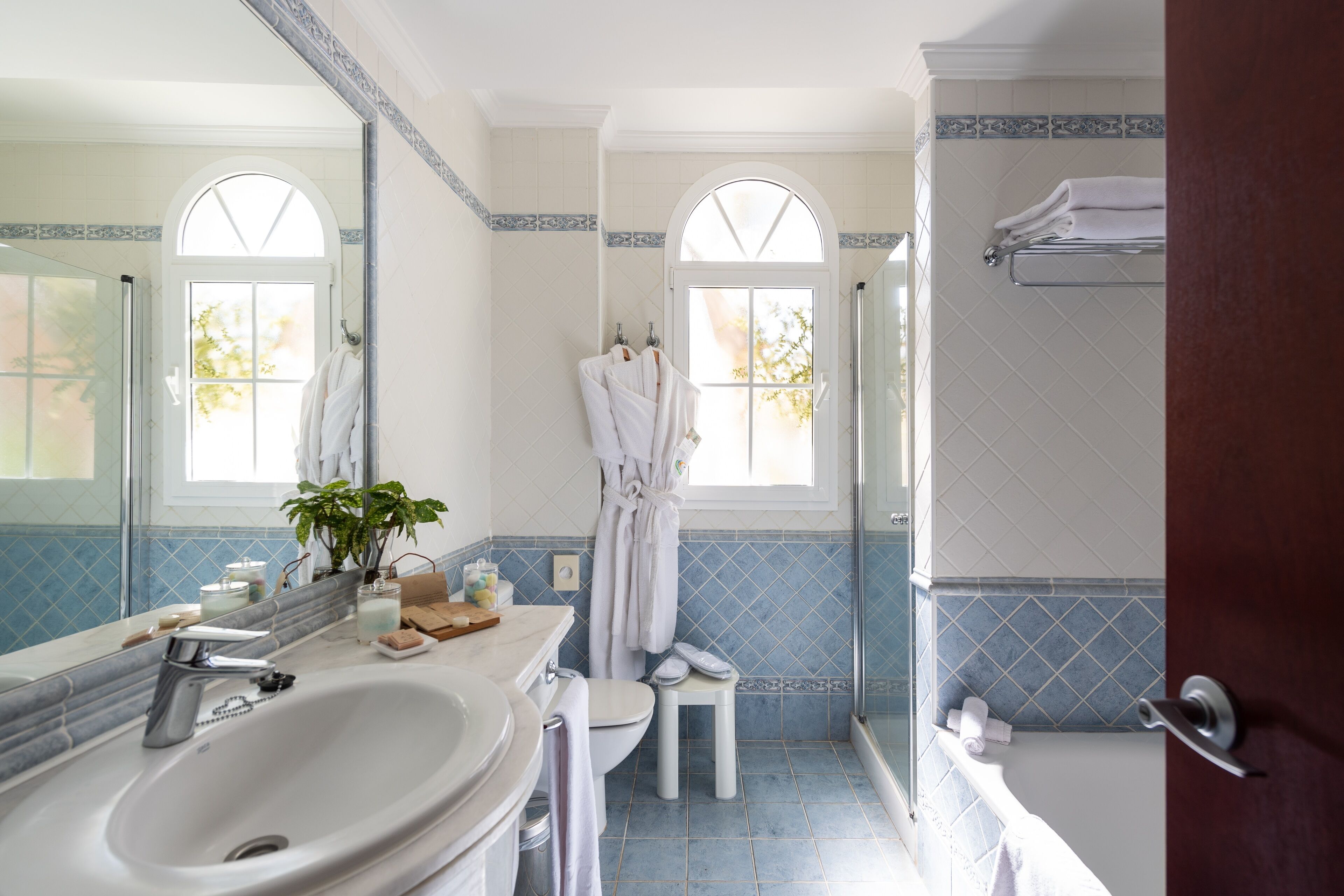 Un baño con un lavamanos grande, inodoro y zona de ducha. Hay toallas y una bata colgadas en la pared.