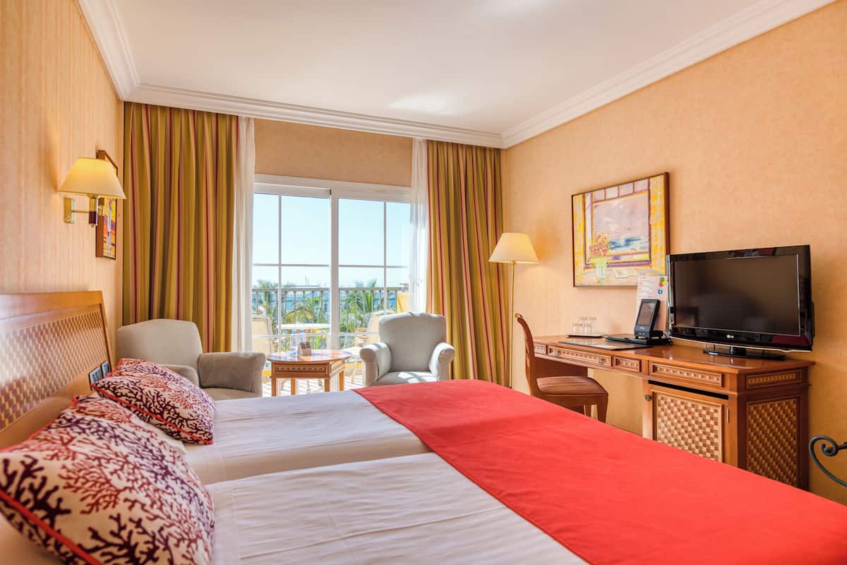 Une chambre d’hôtel avec deux lits, un bureau avec une télévision, une chaise et une vue sur l’extérieur.