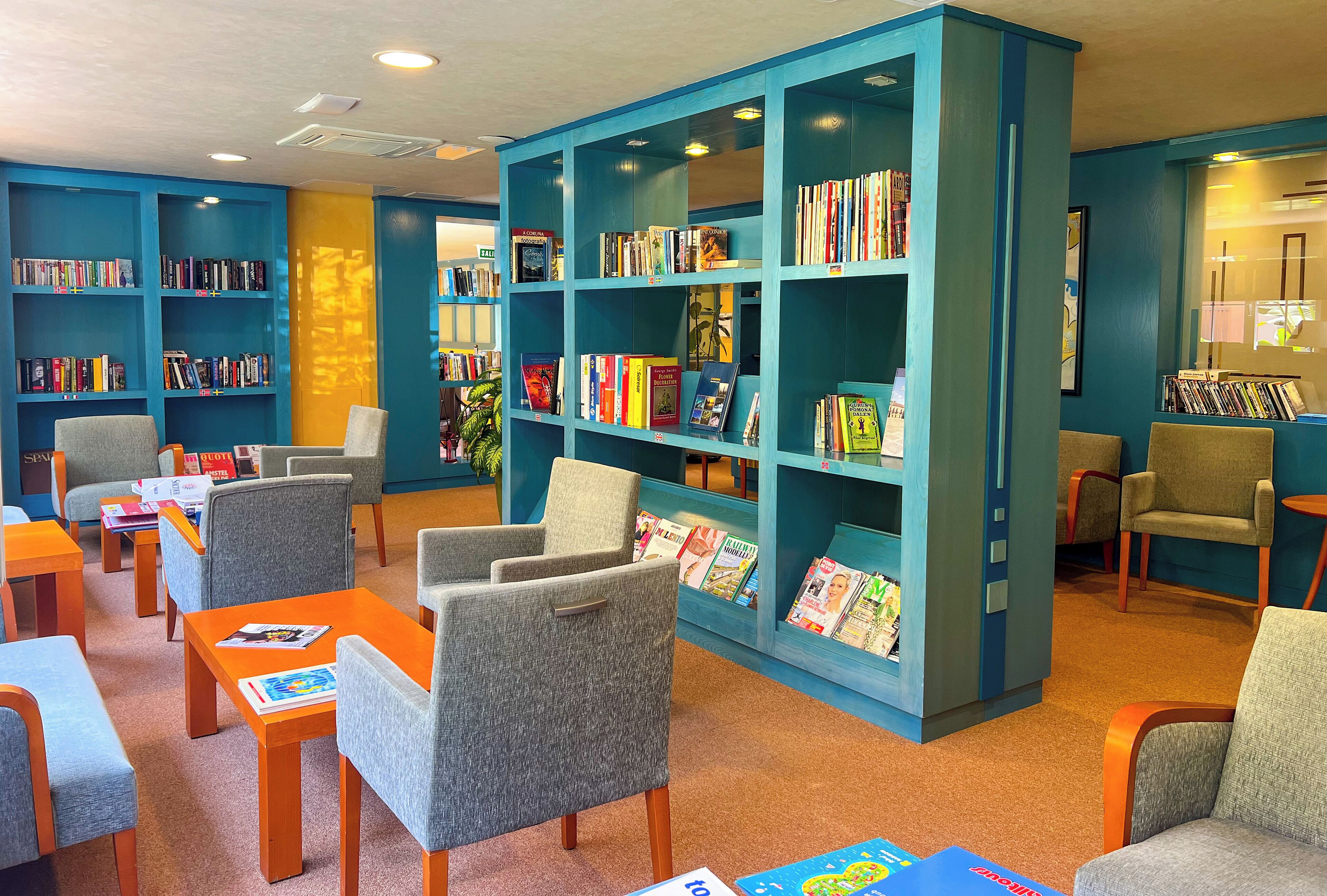 Una biblioteca con estanterías azules, sillas grises y mesas naranjas.