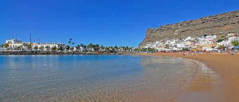 A coastal town with a beach, clear blue water, and buildings on a hillside.