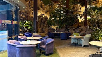 Un espacio interior con asientos, mesas redondas y sillas acolchadas, rodeado de formaciones rocosas y plantas tropicales.