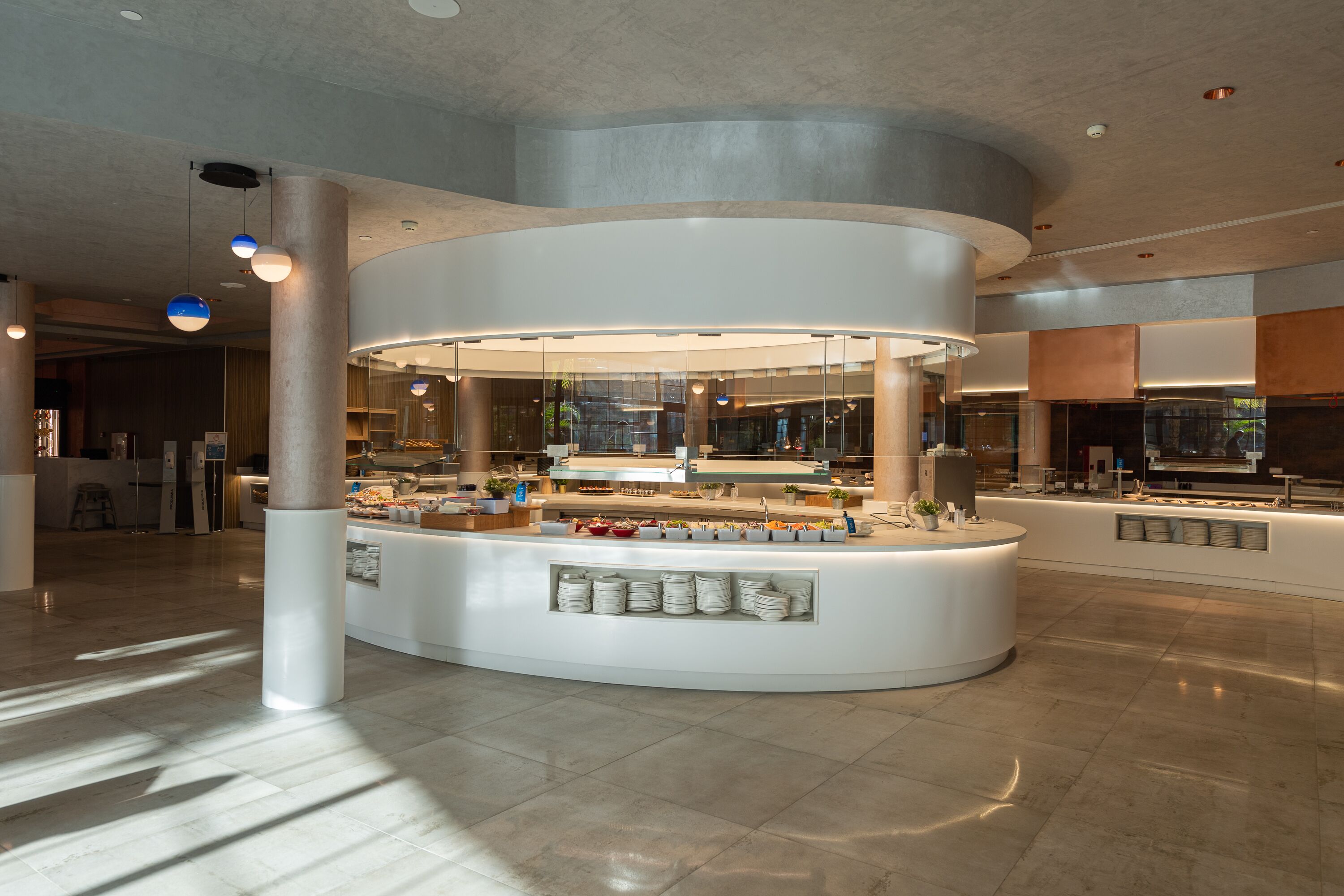 A modern, circular breakfast bar with a central island, surrounded by seating areas and a high ceiling with recessed lighting.