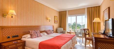 A hotel room with two beds, a TV, a desk, and a view of the outdoors.