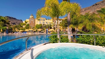 Un resort con piscina, palmeras y montañas al fondo.