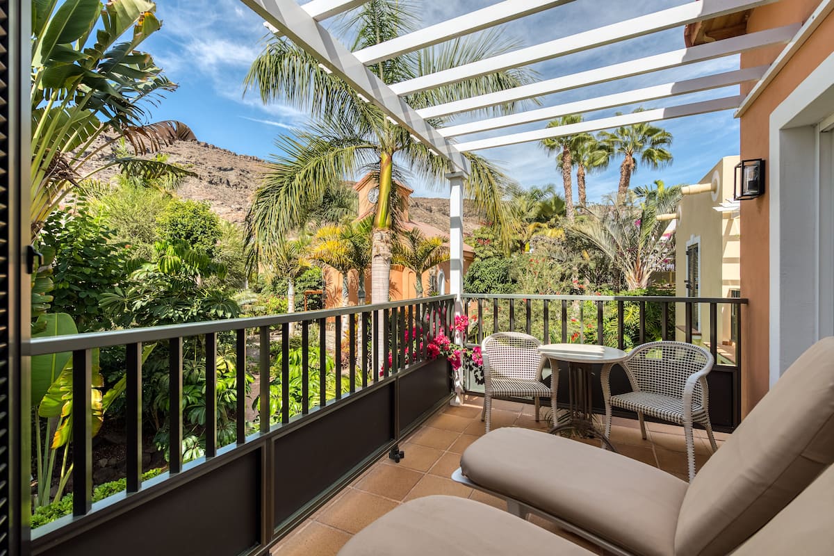 Un balcon avec une balustrade blanche, deux fauteuils en osier, une petite table ronde et un canapé beige.