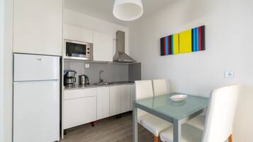 Una cocina moderna con armarios blancos, un microondas, una cafetera y un comedor con mesa de vidrio y sillas blancas.