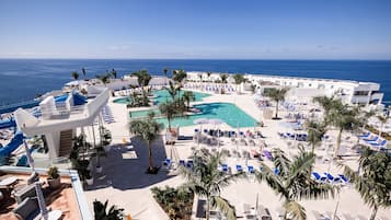 A resort with a pool area, lounge chairs, and palm trees.