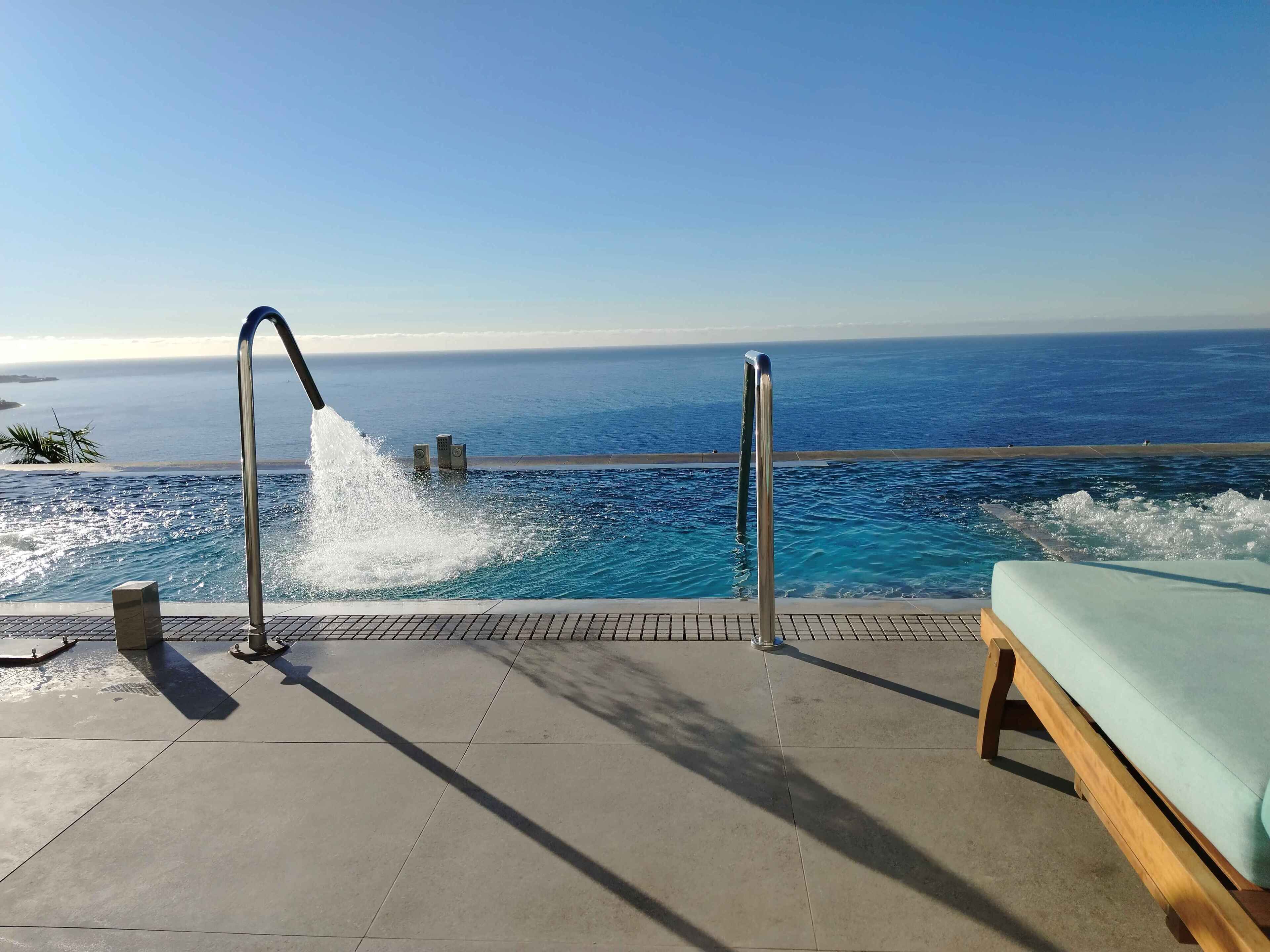 A poolside area with a view of the ocean, a water feature, and a lounge chair.