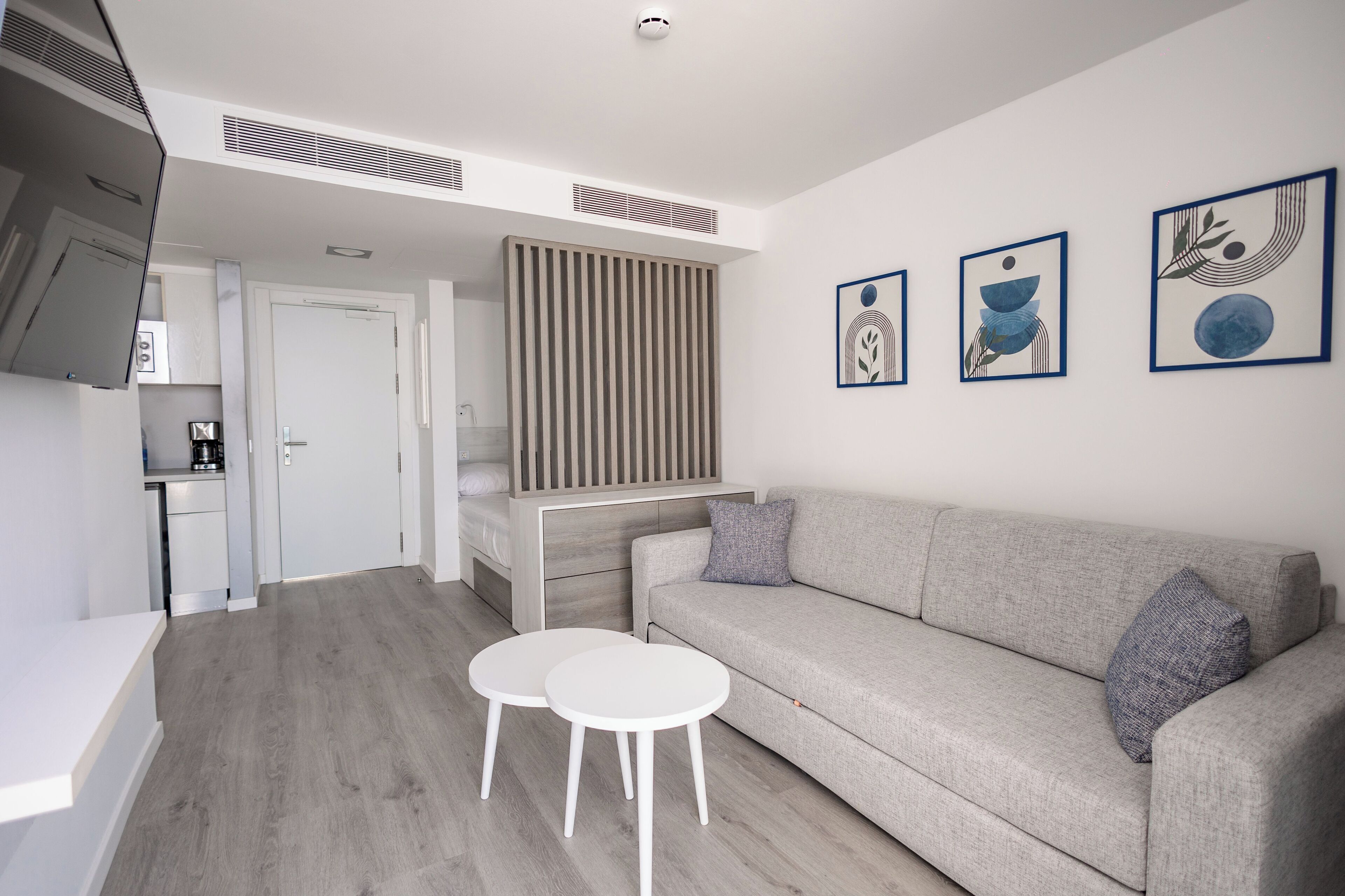 A modern living room with a grey sofa, two white round tables, and a staircase leading to a kitchen area.