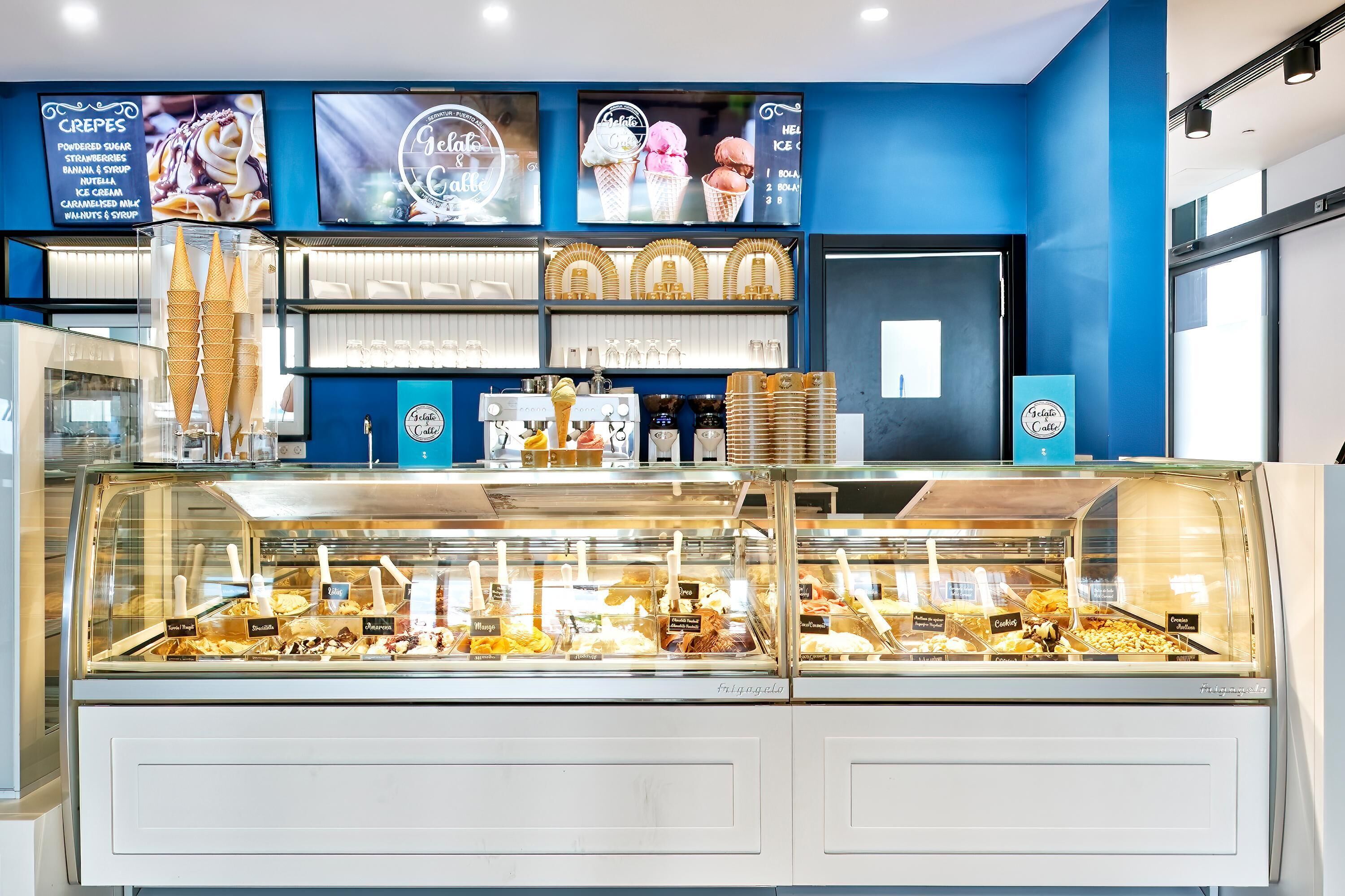 Een ijssalon met een blauwe muur en een glazen vitrine vol verschillende ijssmaken.