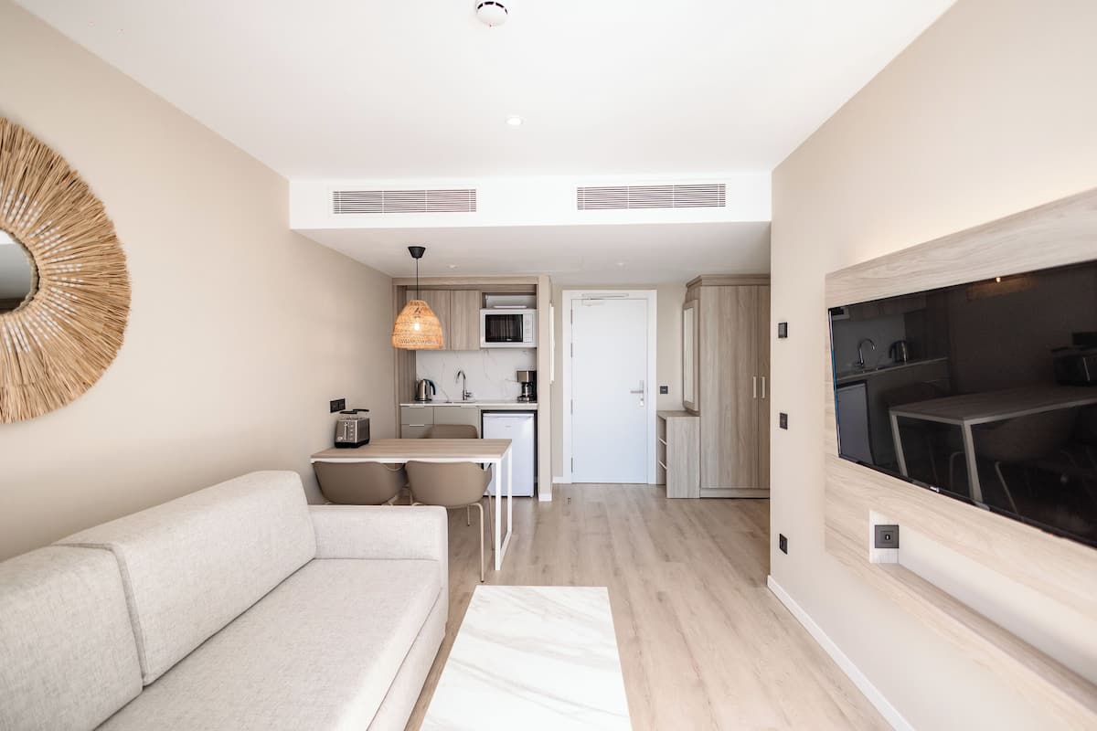 A modern living room with a sofa, a dining area, a kitchen, and a TV mounted on the wall.