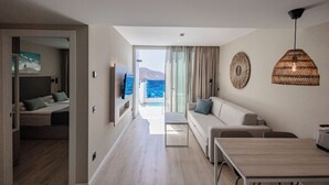 A modern hotel room with a balcony, a sofa, a dining table, and a TV. - Servatur Puerto Azul (Mogan)