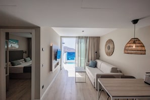 A modern hotel room with a balcony, a sofa, a dining table, and a TV. - Servatur Puerto Azul (Mogan)