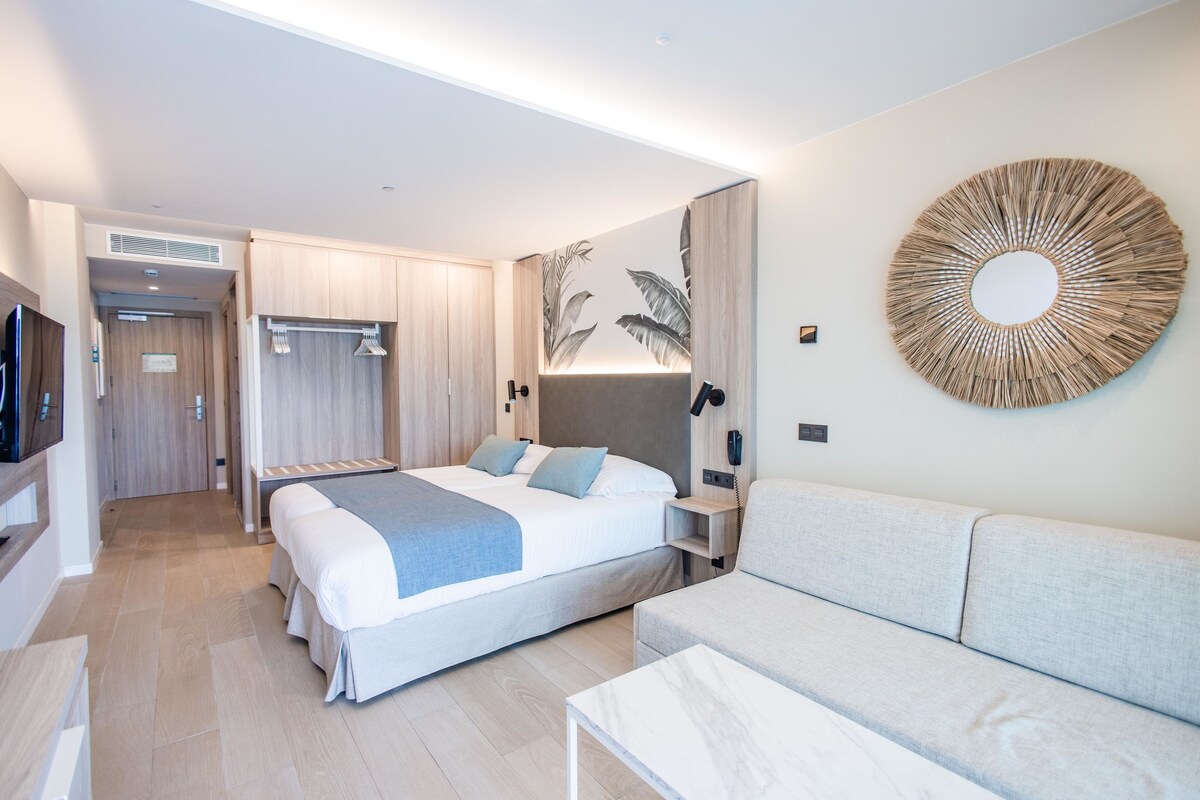 Una habitación de hotel moderna con una cama grande, un sofá, un televisor y un teléfono instalado en la pared.
