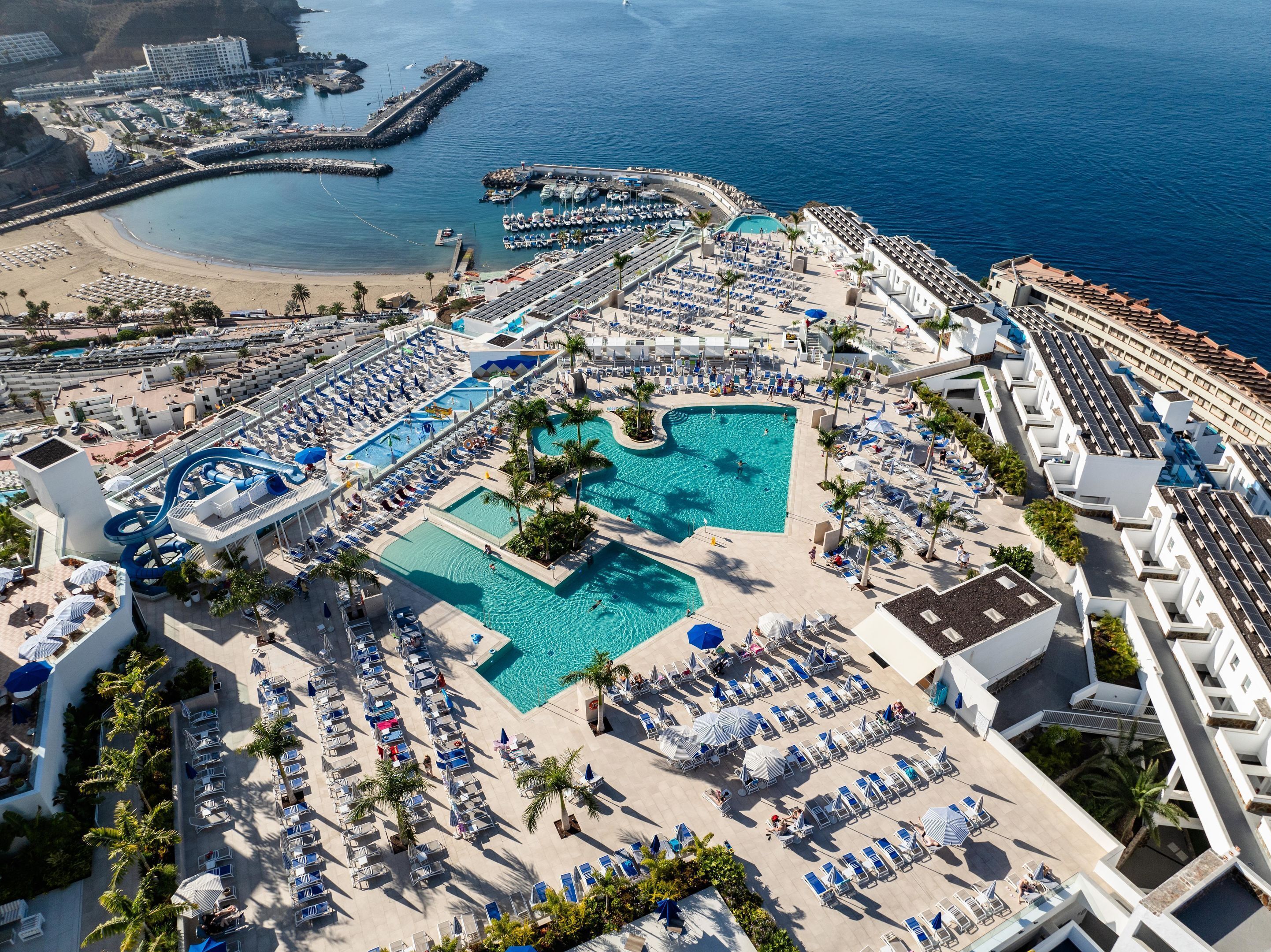 An aerial view of a resort with multiple swimming pools, sun loungers, and a marina.