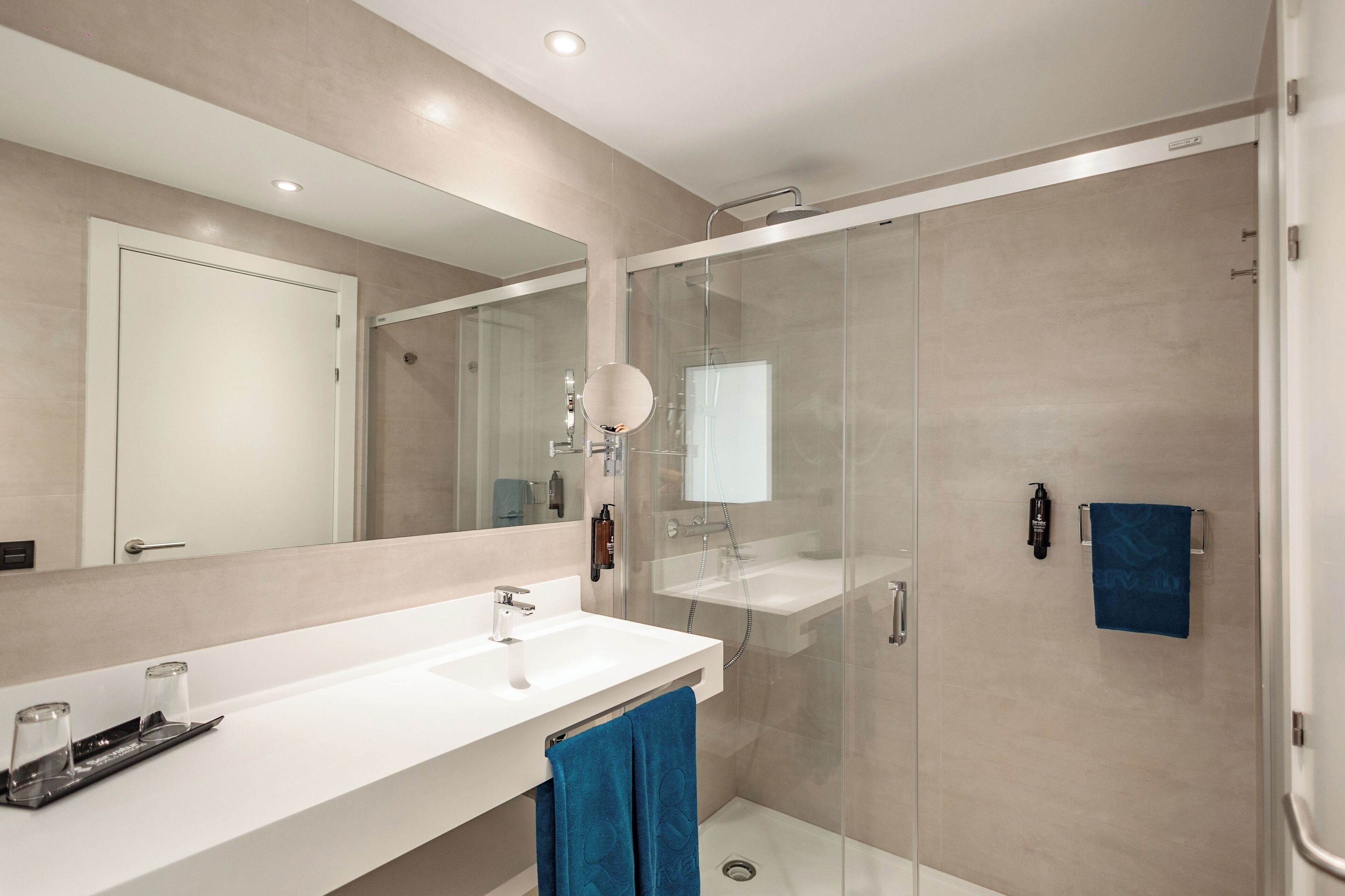 Un baño moderno con ducha de vidrio, un espejo grande y un lavabo blanco.