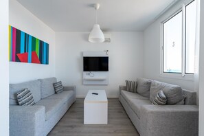 A modern living room with two grey sofas, a white coffee table, a flat-screen TV, and a colorful abstract painting on the wall. - Servatur Puerto Azul (Mogan)