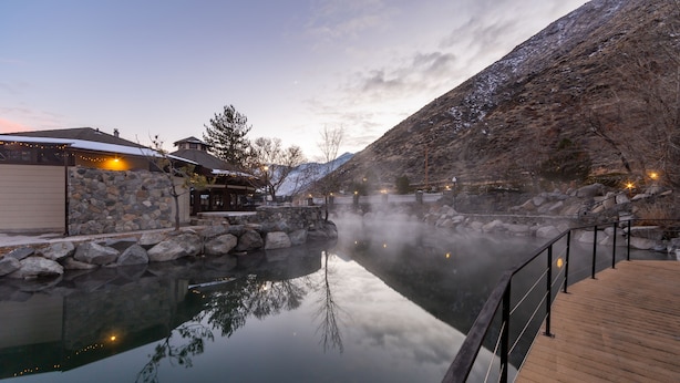 A serene hot spring area with a wooden deck, stone walls, and a building with outdoor seating. - Holiday Inn Club Vacations David Walley's Resort by IHG (Genoa)