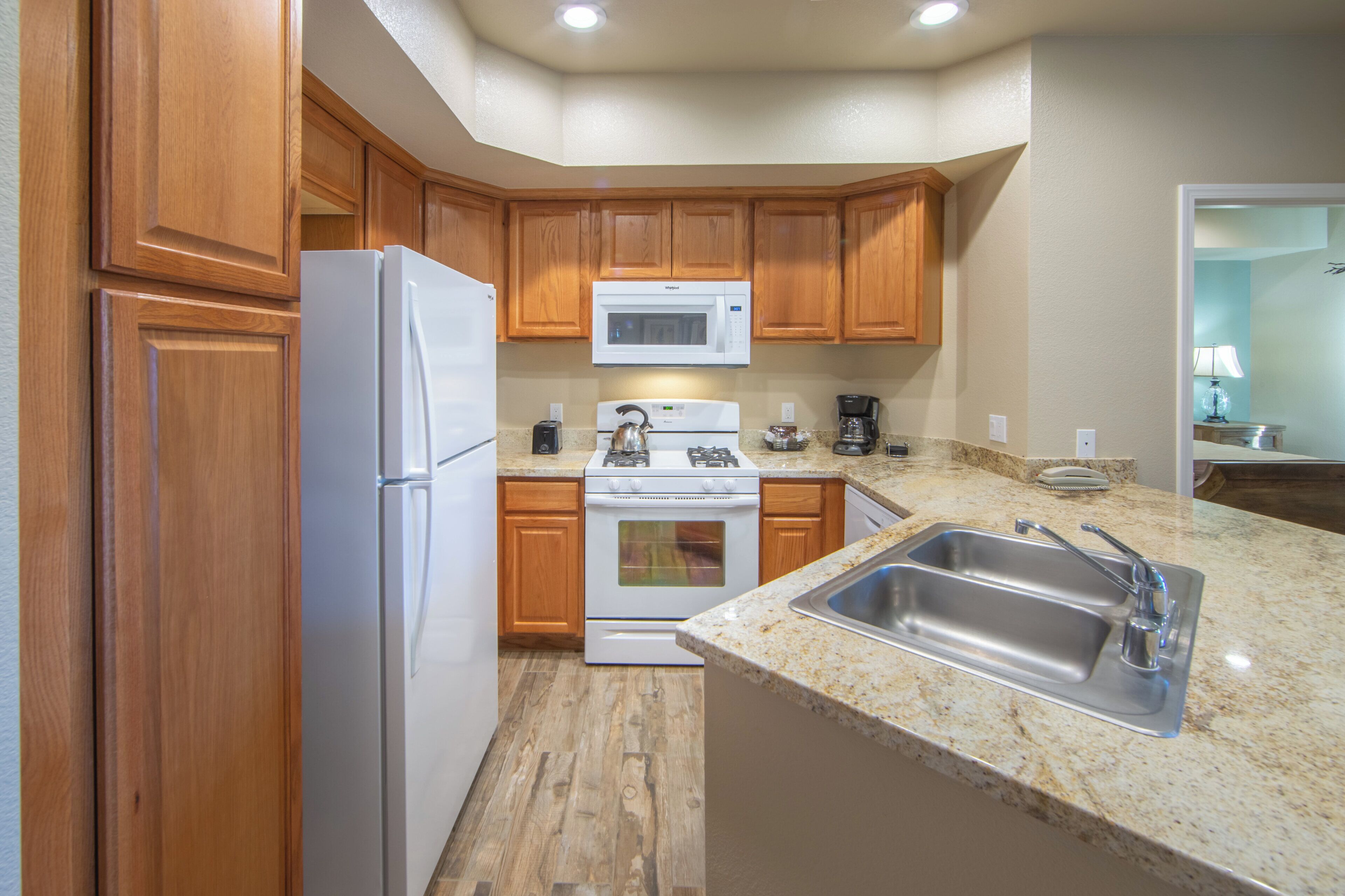 A kitchen with wooden cabinets, a white refrigerator, a microwave, a stove, and a sink.