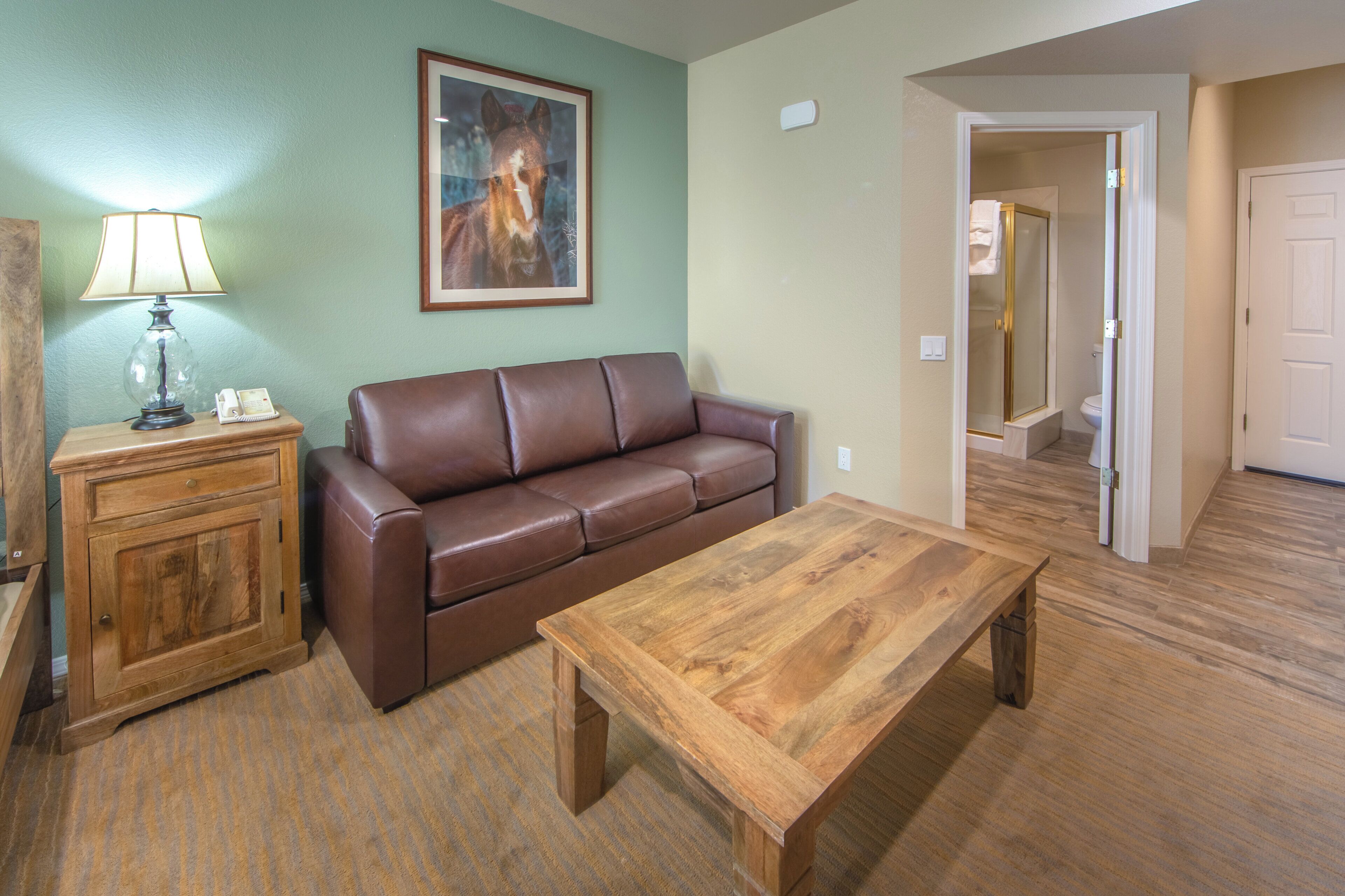 A living room with a brown leather sofa, a wooden coffee table, a lamp, and a framed picture on the wall.