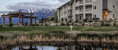 A multi-story building with balconies, a stone retaining wall, and a reflection in a body of water.