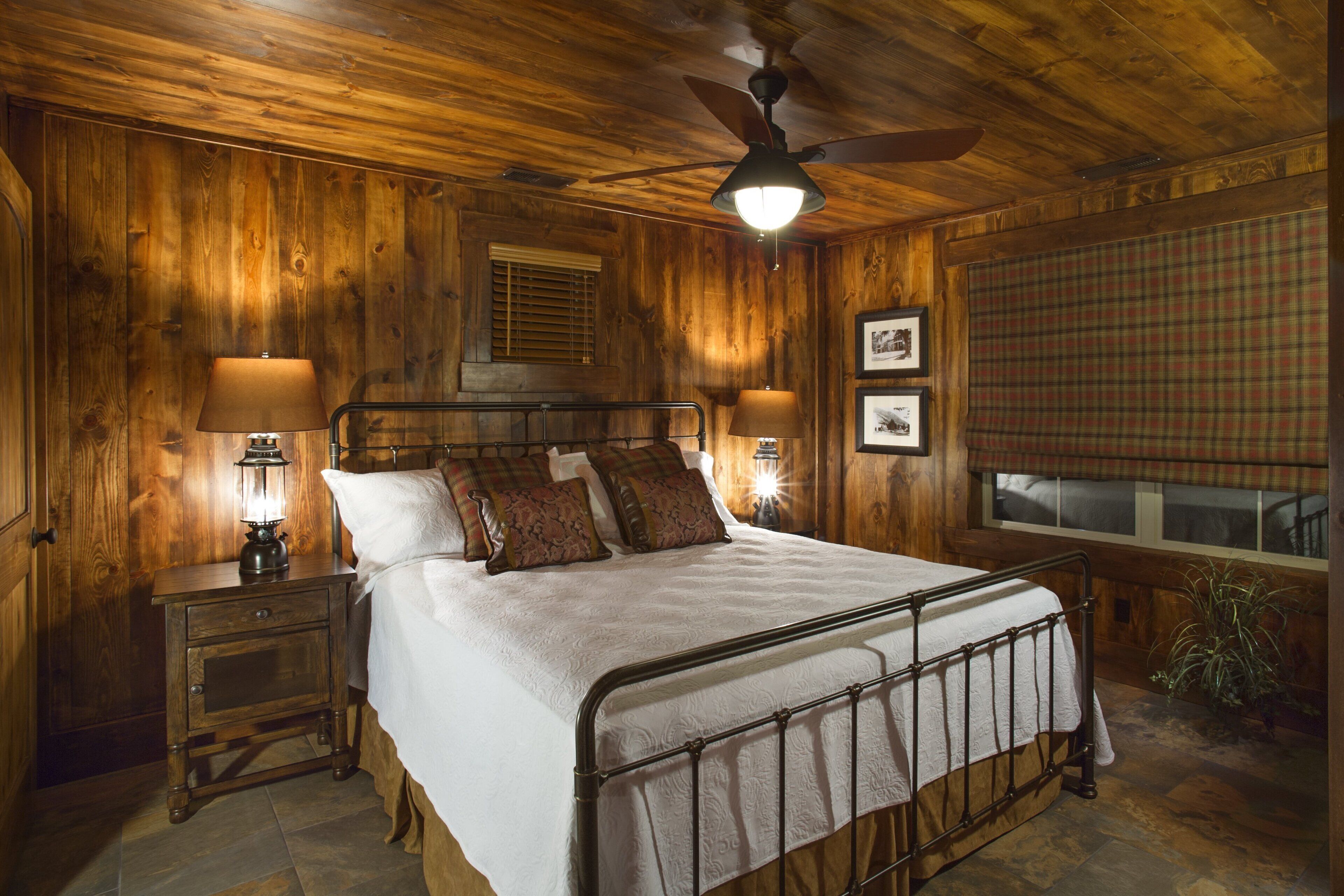 Dormitorio con paneles de madera, una cama, dos lámparas de noche, un ventilador de techo y una ventana con persianas.