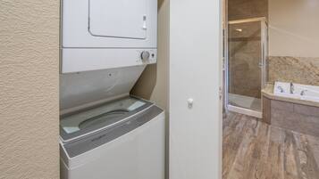 A laundry area with a front-loading washer and dryer, a glass shower enclosure, and a bathroom with a marble countertop and sink.